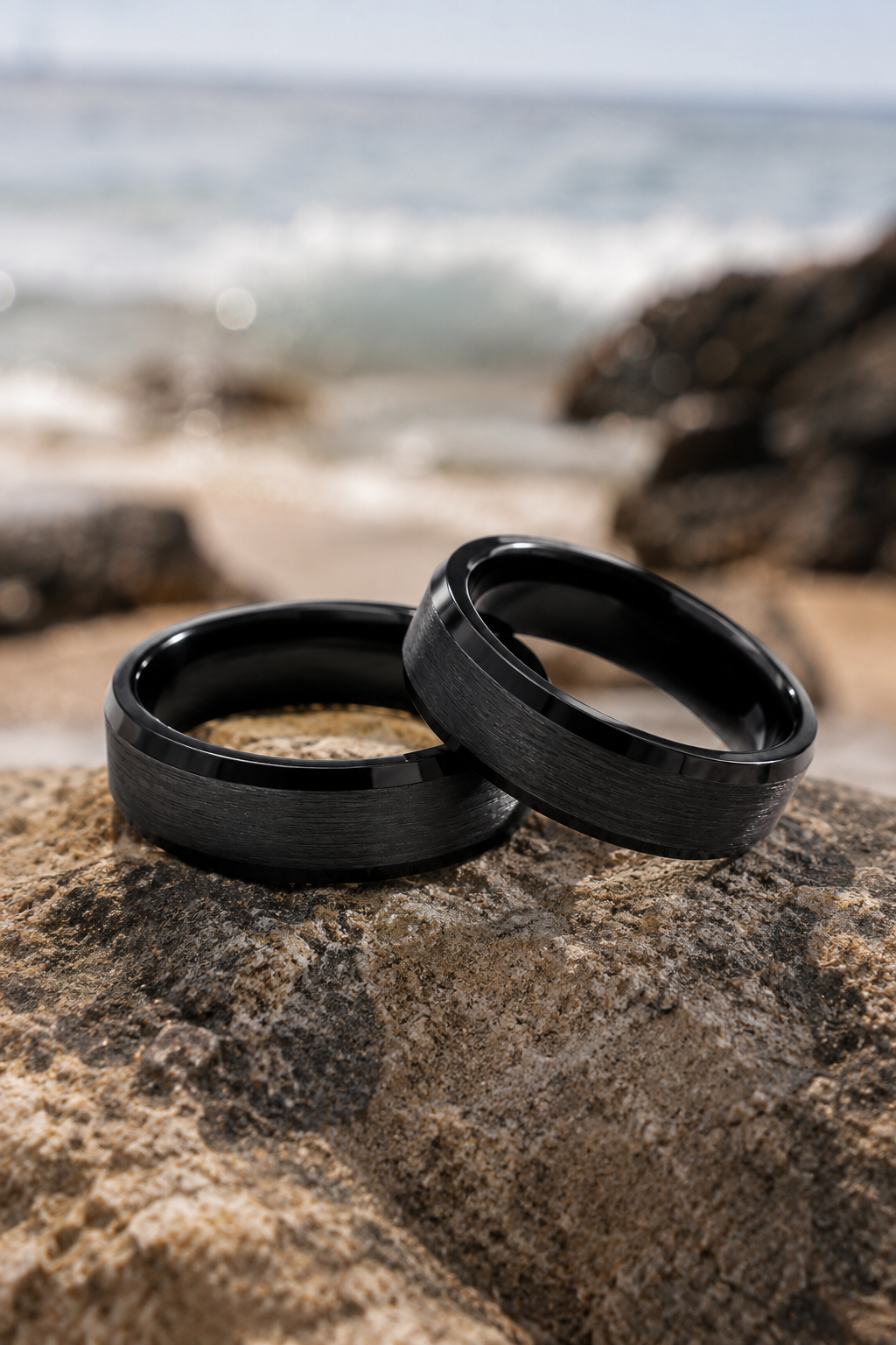 black tungsten rings on rocky beach with ocean background