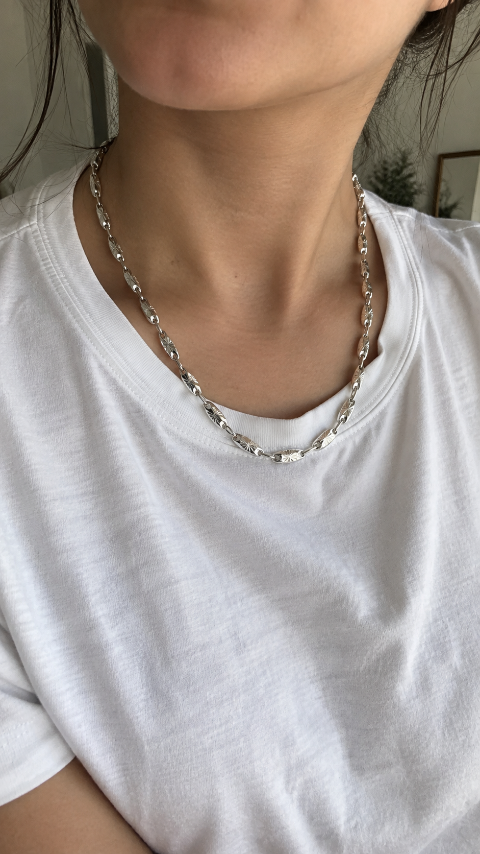 Woman wearing a sterling silver starburst chain necklace with a casual white T shirt in natural window light.