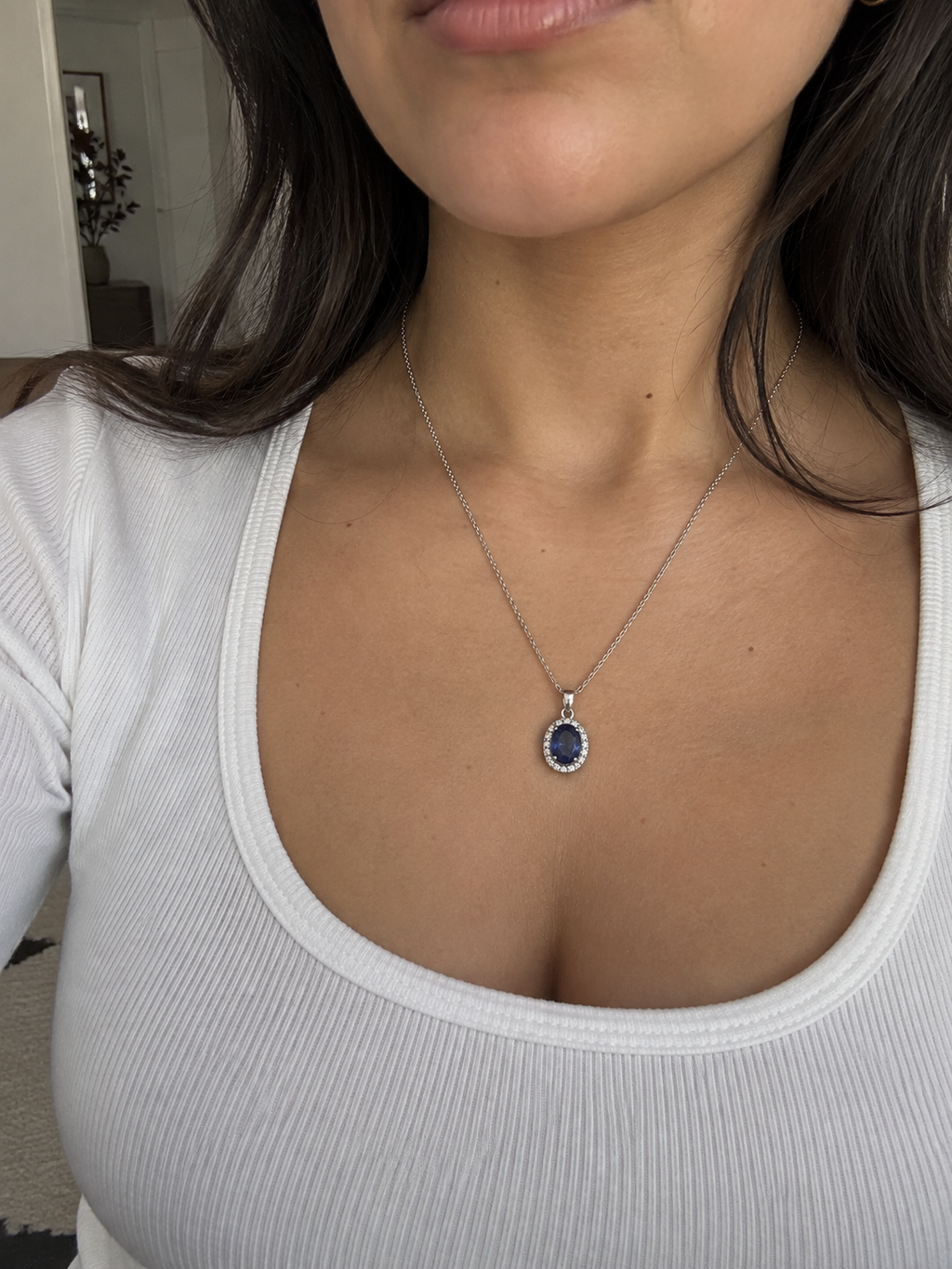 Woman wearing a silver necklace with an oval blue gemstone pendant and sparkling halo setting.